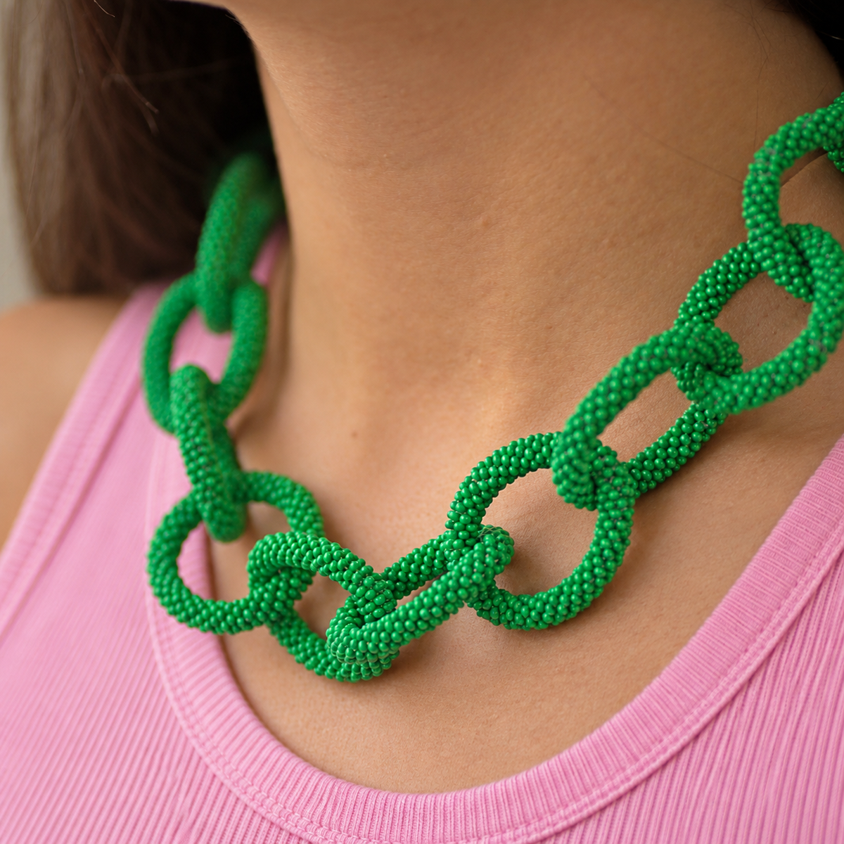 Chunky green beaded statement chain necklace worn with a pink top, showing its oversized textured interlocking links.