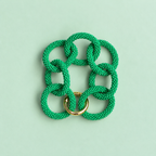 Green chunky beaded chain bracelet with oversized interlocking links and gold tone detail on a pale green background.