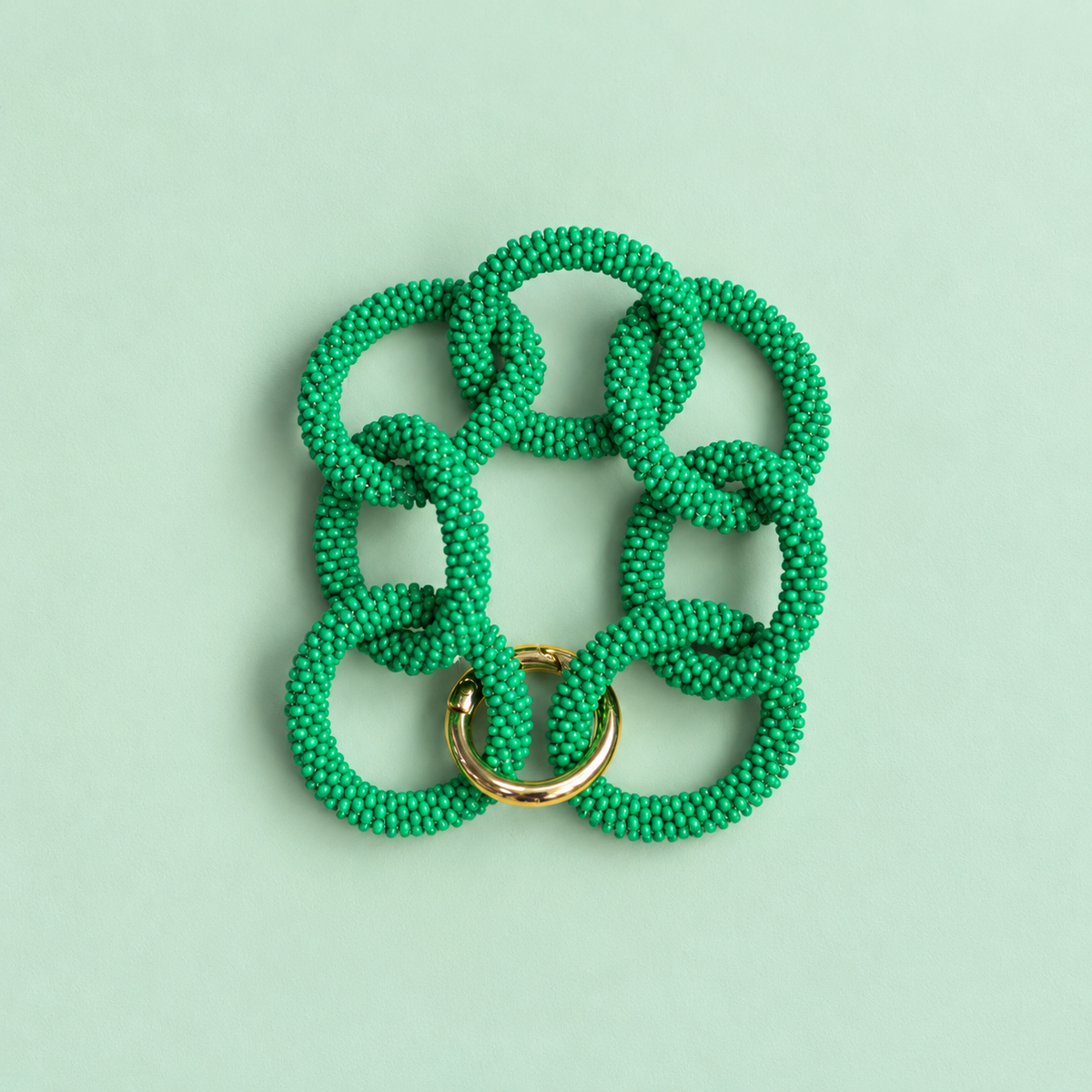 Green chunky beaded chain bracelet with oversized interlocking links and gold tone detail on a pale green background.