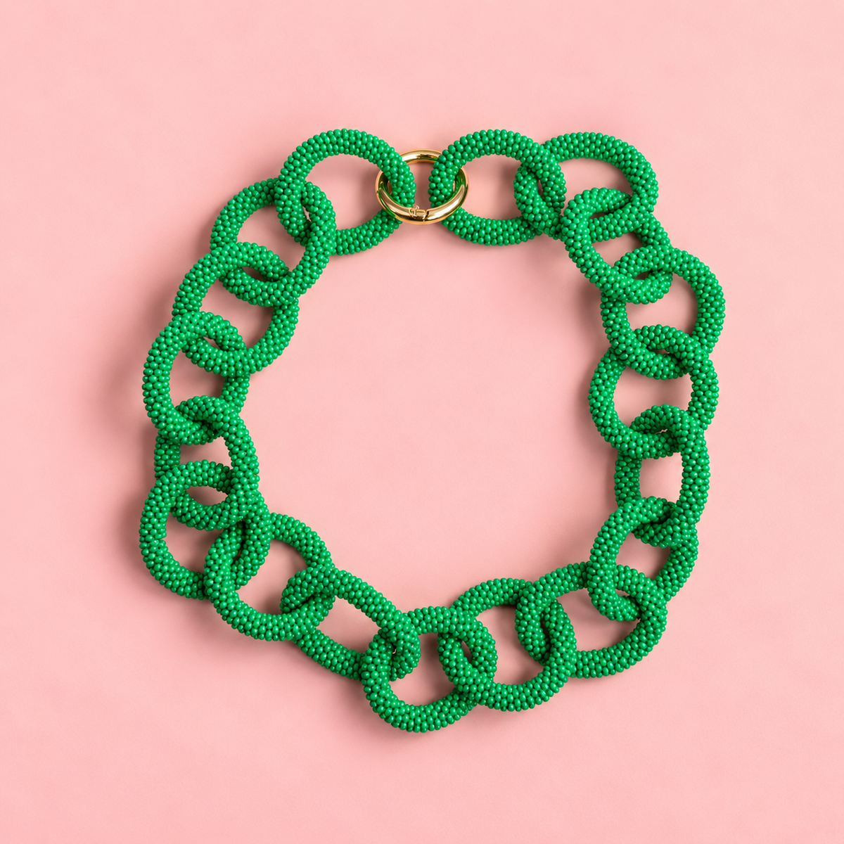 Chunky green beaded statement chain necklace with oversized interlocking links and gold tone ring fastening on a soft pink background.