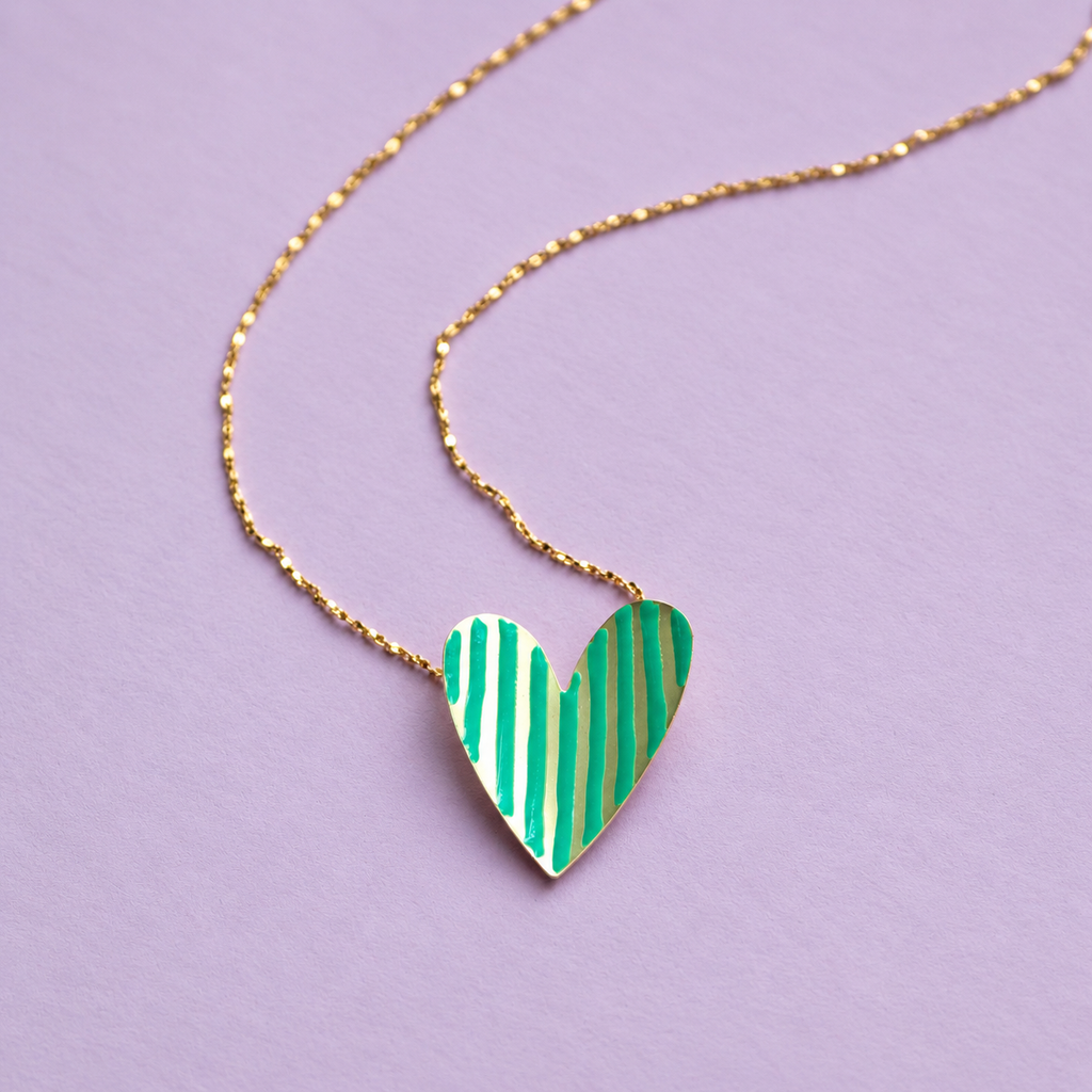 Gold plated heart necklace with bright green enamel stripes on a delicate adjustable chain, photographed on a lilac background.