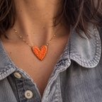 Woman wearing an orange and white polka dot enamel heart necklace with a grey denim shirt.
