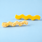 Pair of yellow wave hair slides, one marbled yellow and cream and one bright yellow, on a pale blue background.