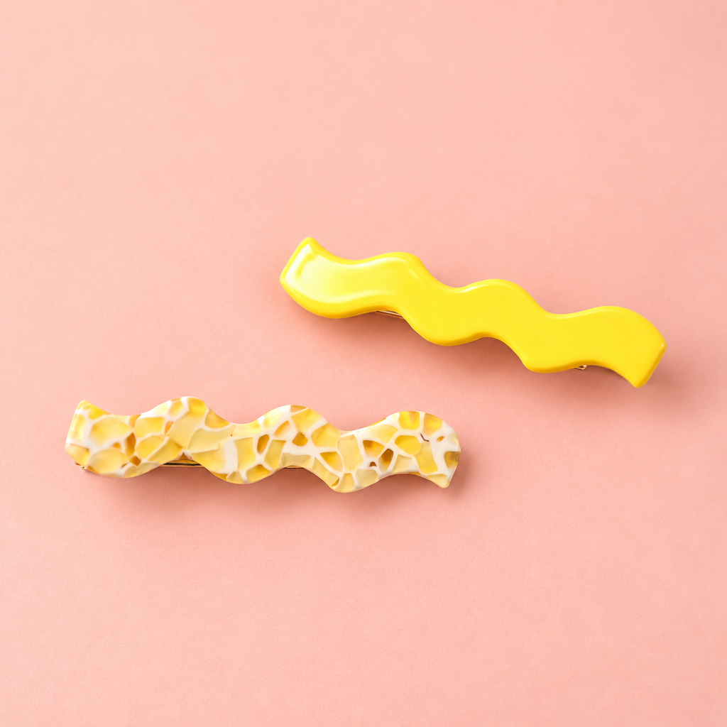 Yellow wave hair slide set featuring one bright yellow and one marbled yellow and cream design on a soft pink background.