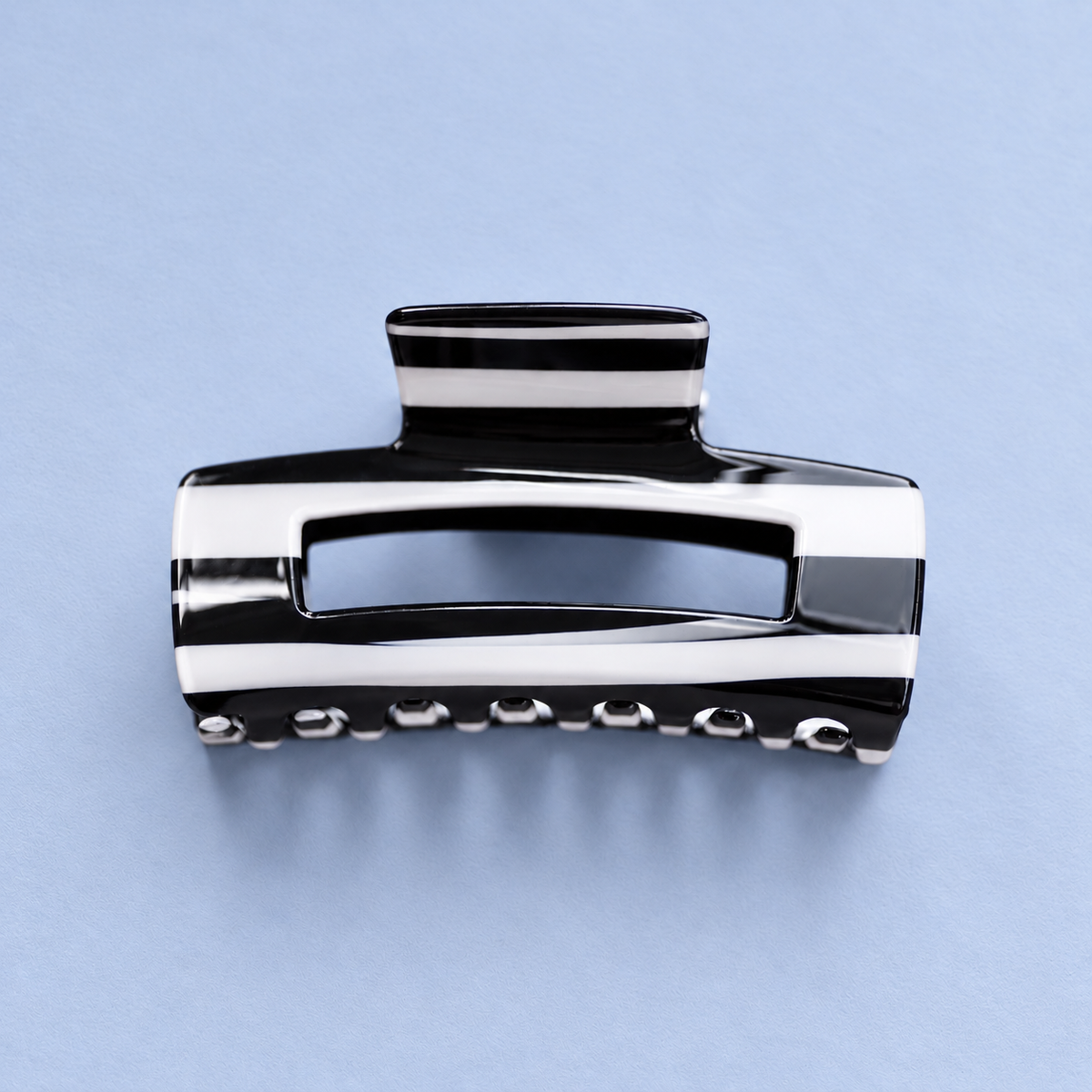 Black and white striped acrylic claw hair clip with a glossy finish on a soft pale blue background.