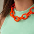Chunky orange beaded statement chain necklace worn with a mint green top, showing its oversized textured interlocking links.