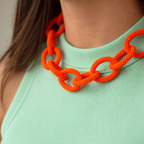 Chunky orange beaded statement chain necklace worn with a mint green top, showing its oversized textured interlocking links.