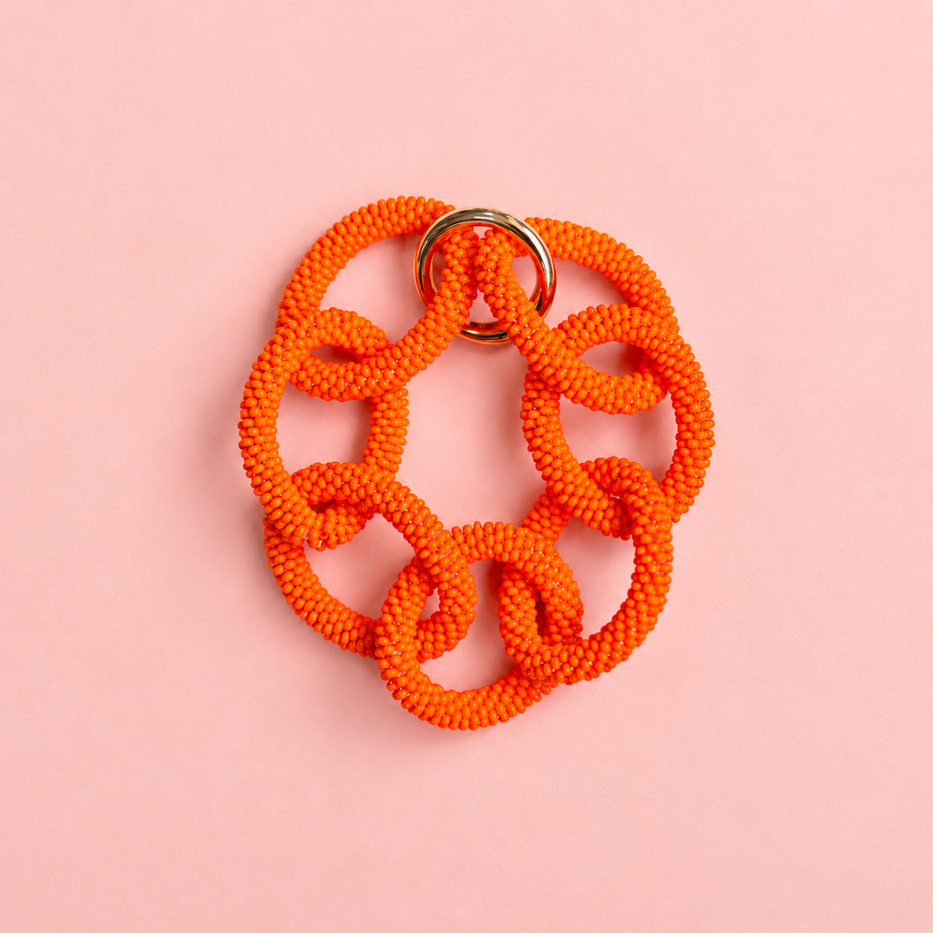 Chunky orange beaded statement chain bracelet with oversized interlocking links on a soft pink background.
