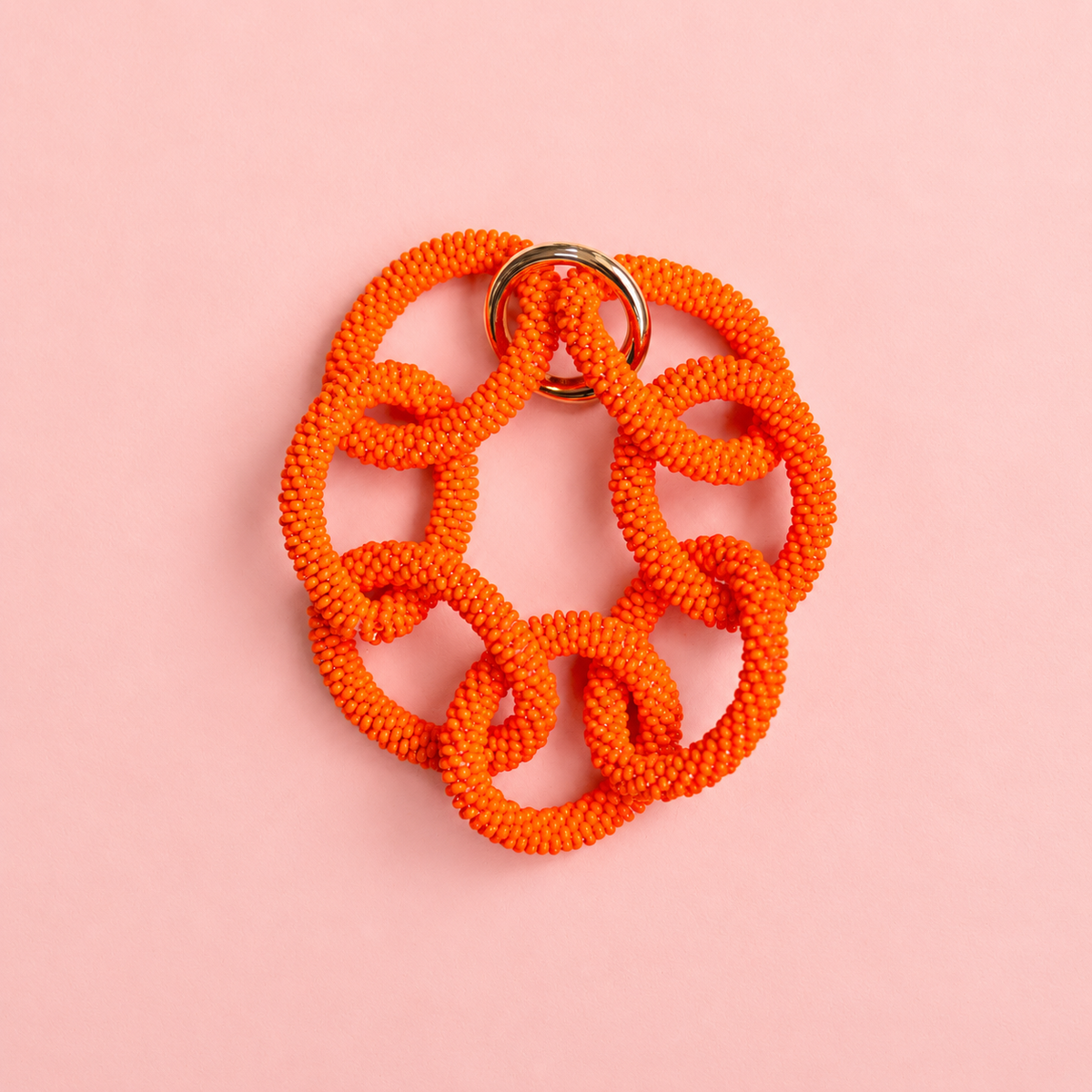 Chunky orange beaded statement chain bracelet with oversized interlocking links on a soft pink background.