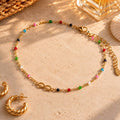 Gold tone infinity anklet with tiny multicoloured beads displayed on a neutral stone background.
