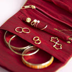 Open red velvet jewellery travel pouch showing zipped compartments, ring storage and gold jewellery inside.