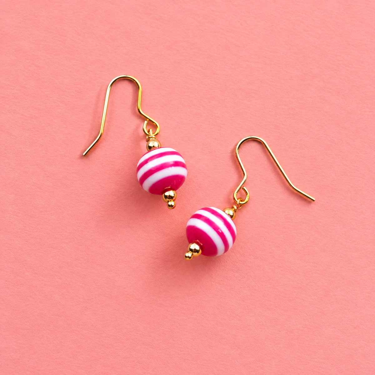 Limited edition pink and white striped retro acrylic drop earrings with gold tone hooks on a coral pink background.