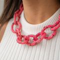 Chunky pink mix beaded statement chain necklace worn with a white knit top, showing its oversized textured interlocking links.