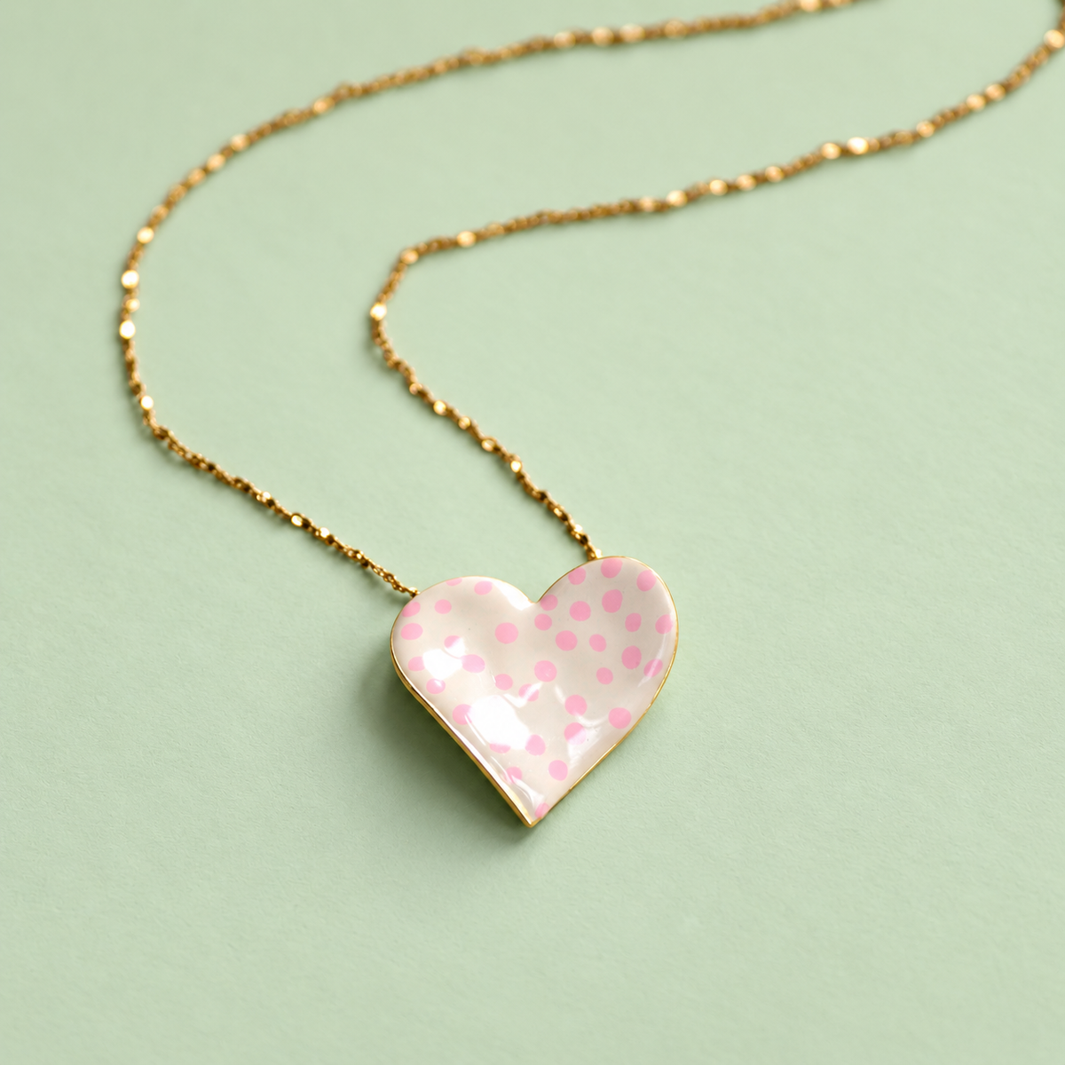 Limited edition gold plated heart necklace with cream enamel and pink polka dots on a soft pale green background.