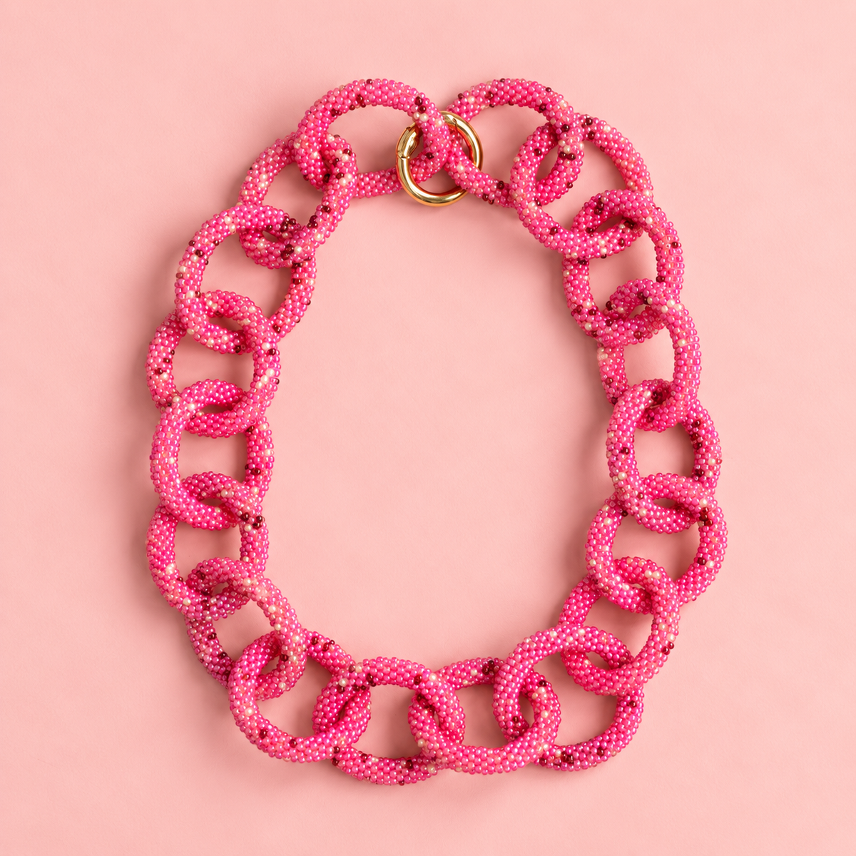 Chunky pink mix beaded statement chain necklace with oversized interlocking links and gold tone ring fastening on a soft pink background.