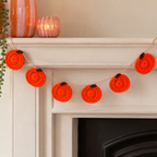 Handmade orange crochet pumpkin garland draped across a fireplace mantel with colourful autumn accessories.