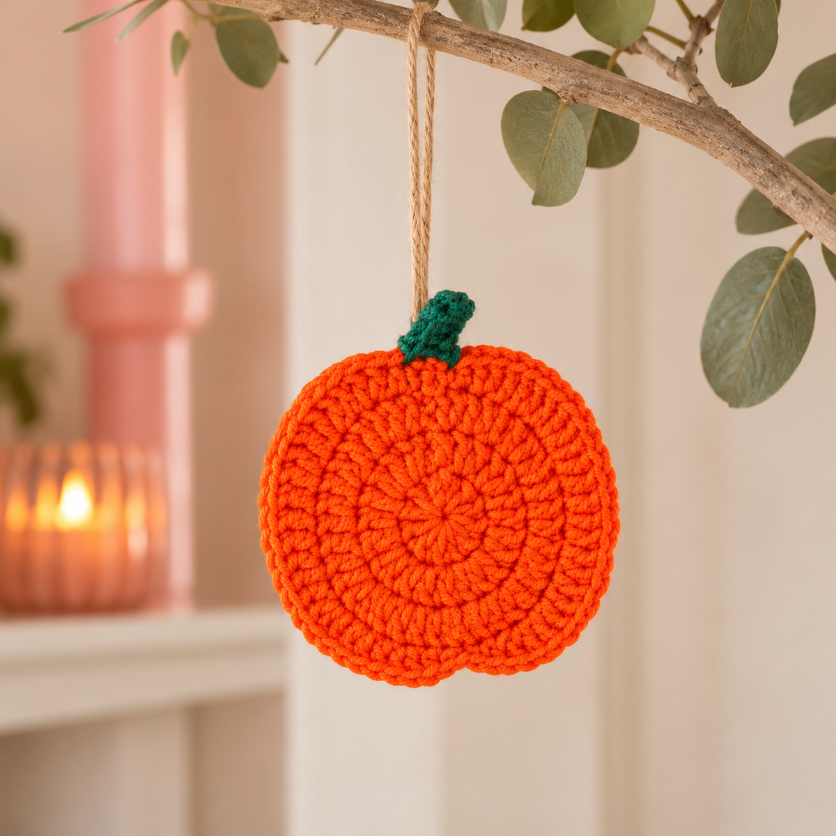 Handmade orange crochet pumpkin with green stalk used as a hanging autumn decoration.