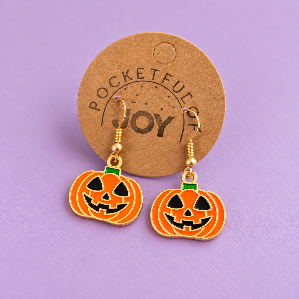 Orange Halloween pumpkin drop earrings displayed on a Pocketful of Joy card against a lilac background.