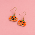 Orange enamel jack o’ lantern pumpkin drop earrings with black, green and gold coloured detailing on a pink background.