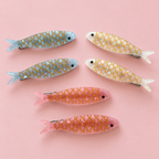Two pink glitter sardine hair clips with gold scale detailing beside a vintage style sardine tin.
