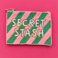 Pink and green diagonally striped beaded pouch with white Secret Stash lettering, gold detailing and gold zip on a bright pink background.