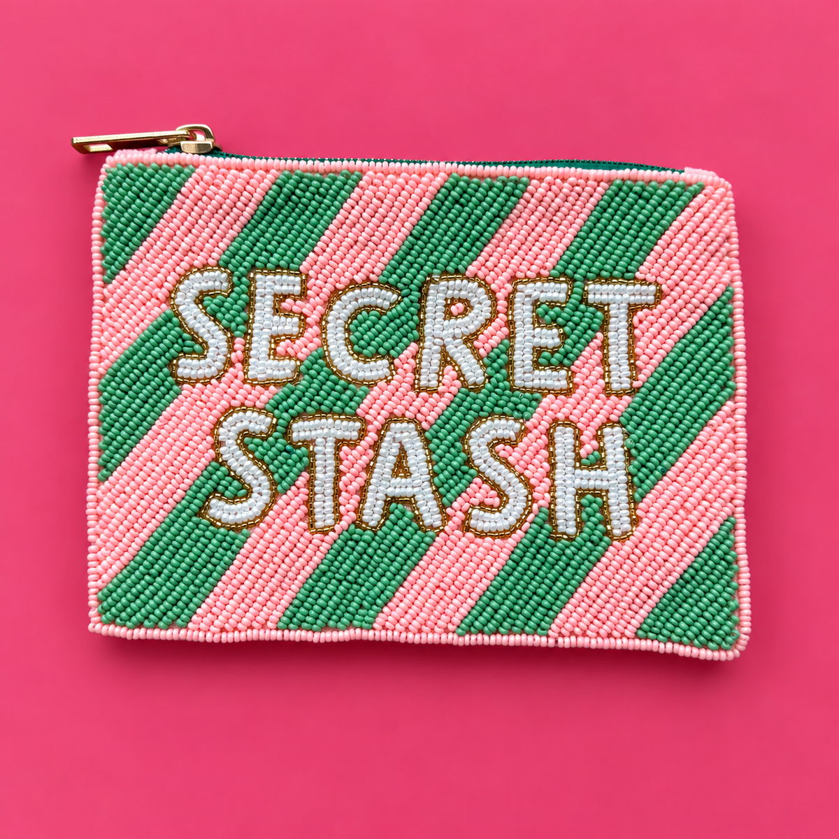 Pink and green diagonally striped beaded pouch with white Secret Stash lettering, gold detailing and gold zip on a bright pink background.