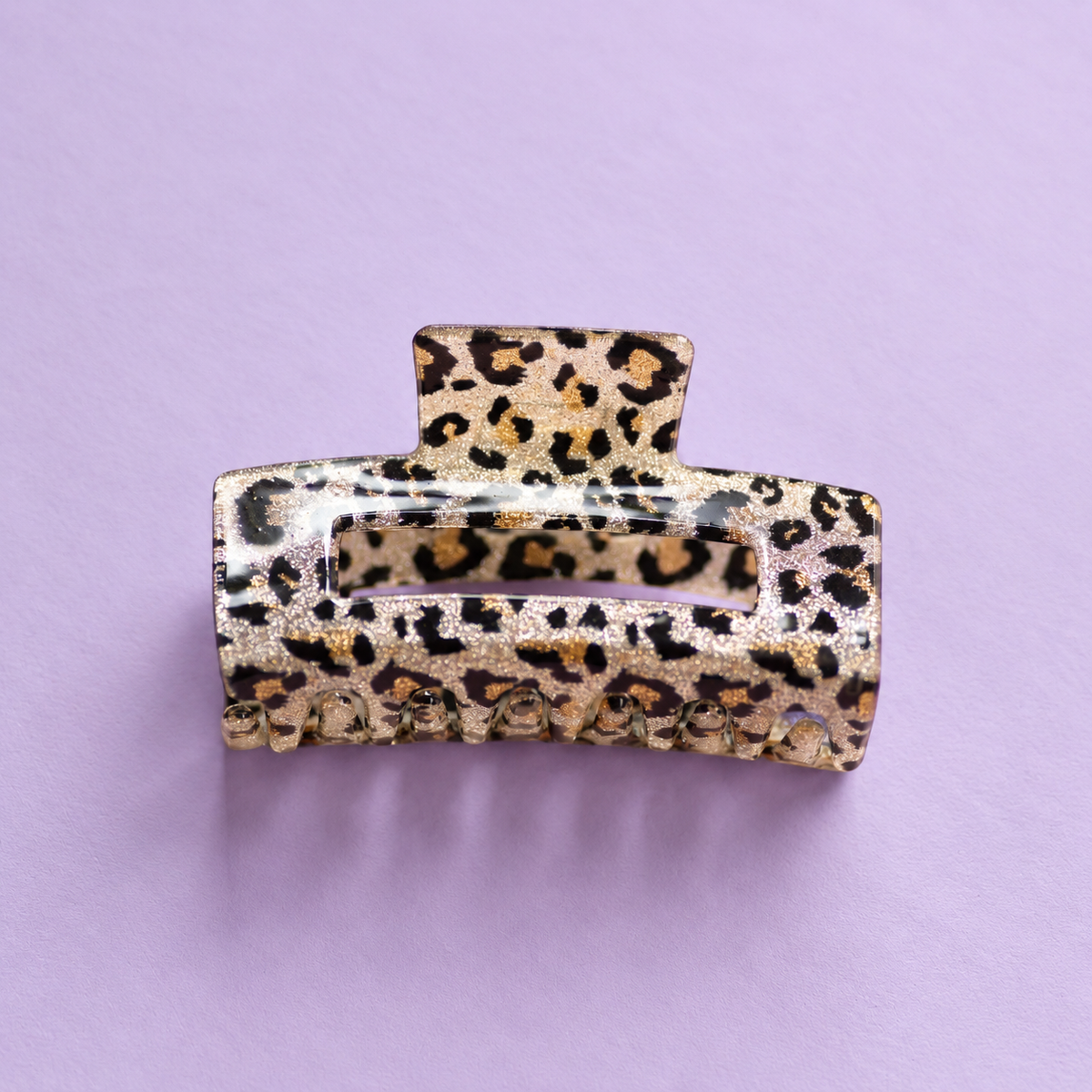 Sparkly leopard print acrylic claw hair clip with black and gold detailing on a soft lilac background