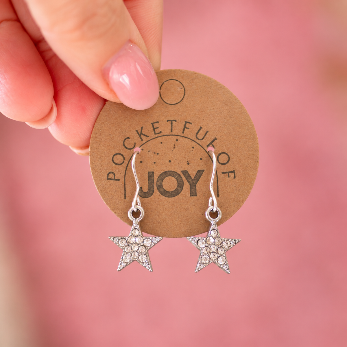 Pair of silver tone crystal star drop earrings held on a Pocketful of Joy display card.