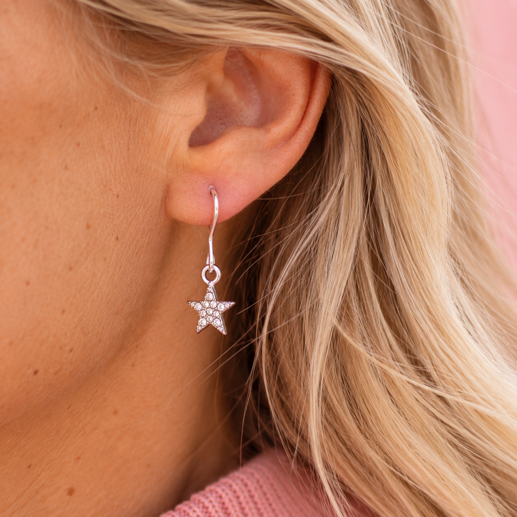 Close up of a silver tone sparkling star drop earring being worn.