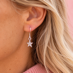 Close up of a silver tone sparkling star drop earring being worn.