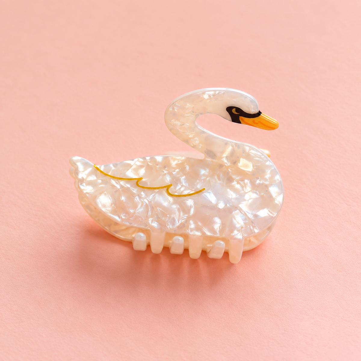 Pearlescent white swan shaped acrylic claw hair clip with gold detailing and orange beak on a soft peach pink background.