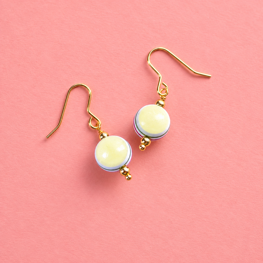 Retro yellow and multicoloured striped acrylic drop earrings with gold tone hooks on a soft coral pink background.